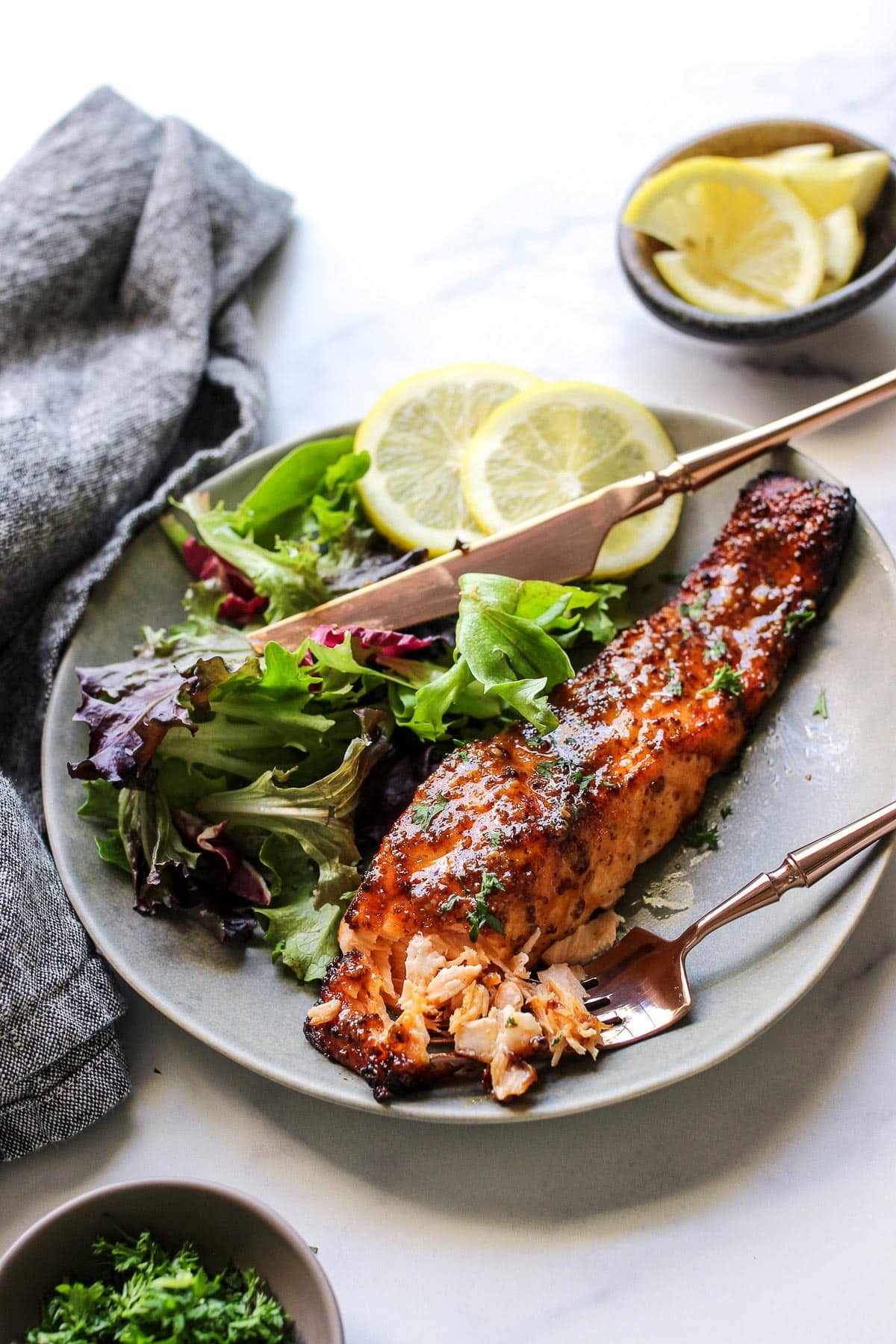 A flaked air fryer honey mustard salmon fillet on a plate with a leafy salad and two lemon slices.