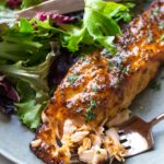 A flaked air fryer honey mustard salmon fillet on a plate with a leafy salad and two lemon slices.