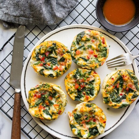 Healthy egg white muffin breakfast cups on a white plate with hot sauce.