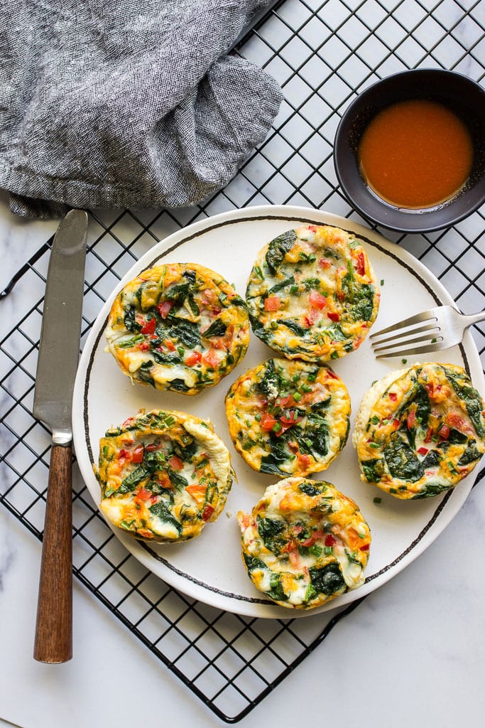 Healthy egg white muffin breakfast cups on a white plate with hot sauce.