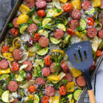 A sheet pan of sausage and veggies with parsley and parmesan cheese.