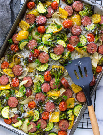 A sheet pan of sausage and veggies with parsley and parmesan cheese.