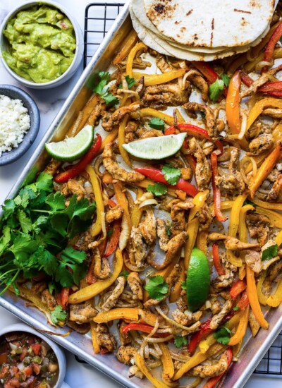 Some chicken fajitas in a sheet pan with onions, bell peppers, cilantro and lime wedges.