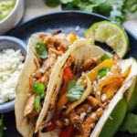 A plate of two chicken fajitas topped with cilantro, lime juice and queso fresco.