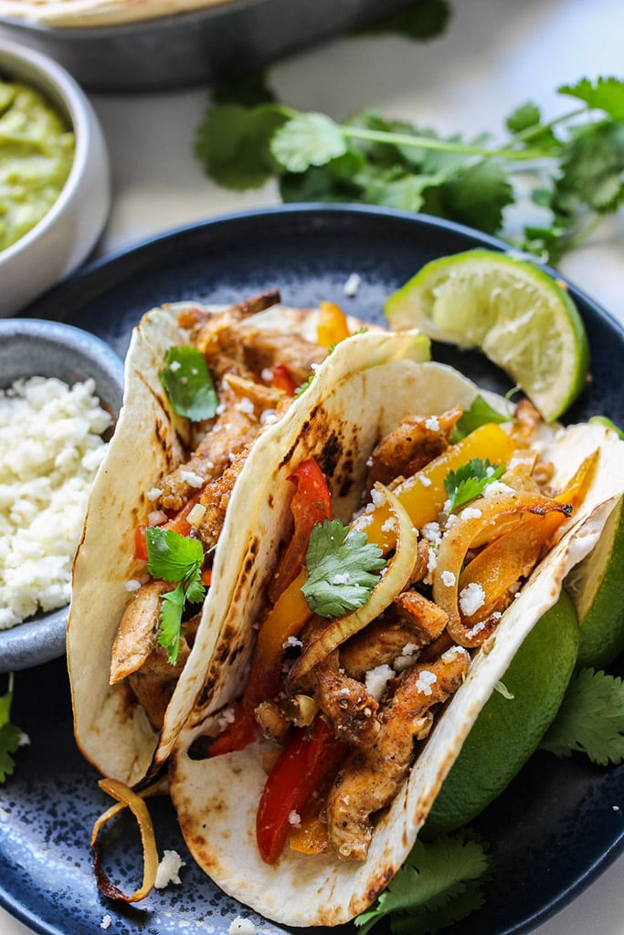 A plate of two chicken fajitas topped with cilantro, lime juice and queso fresco.