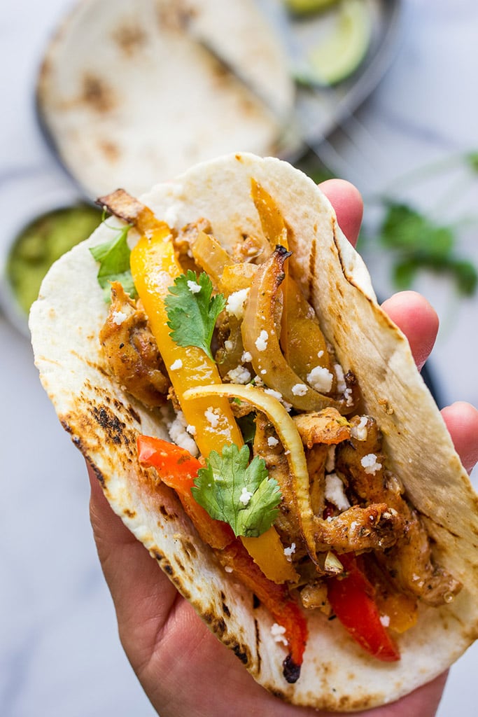 A hand holding a toasted tortilla stuffed with chicken fajitas, onions and bell peppers.