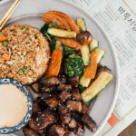 Hibachi rice, veggies and steak on a white plate with a side of Yum Yum sauce.