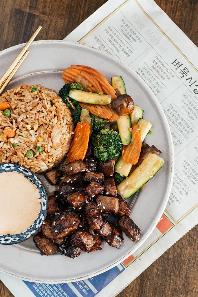 Hibachi rice, veggies and steak on a white plate with a side of Yum Yum sauce.