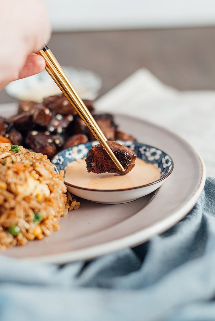 A pair of gold and black chopsticks holding a piece of hibachi steak while dipping into a bowl of Yum Yum sauce.