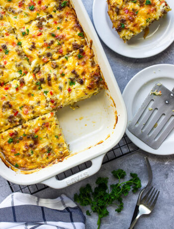 Cheesy sausage hash brown breakfast casserole in a white casserole dish with a slice missing.