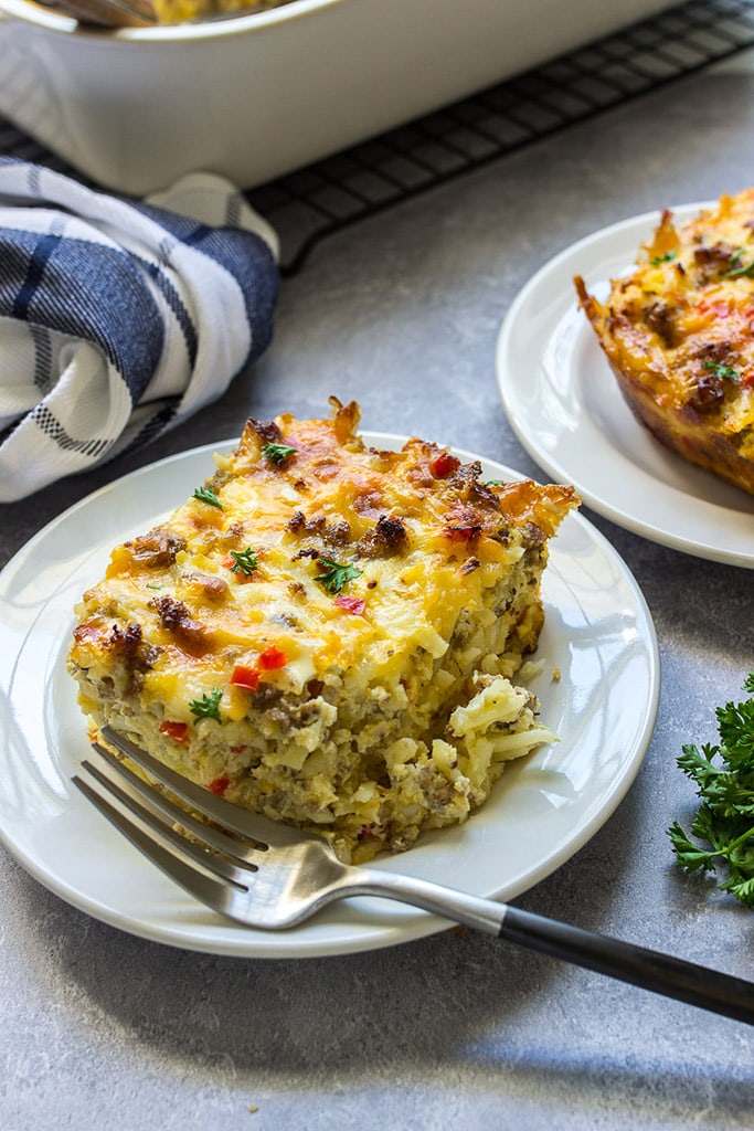 Two slices of hash brown breakfast casserole on white plates.