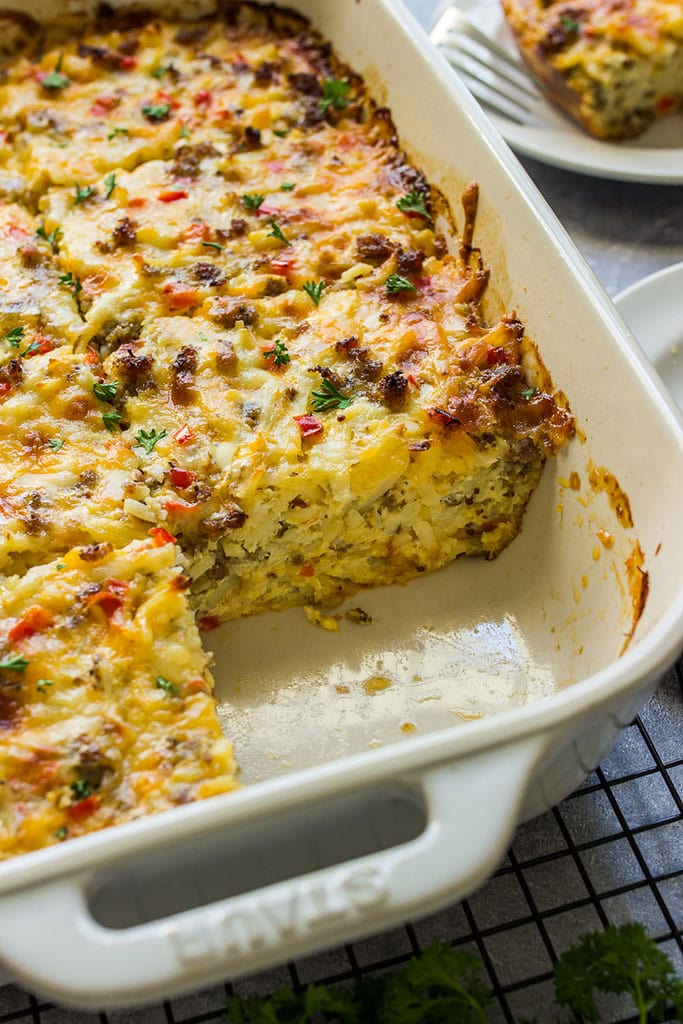 Cheesy sausage hash brown breakfast casserole in a white casserole dish with a slice missing.