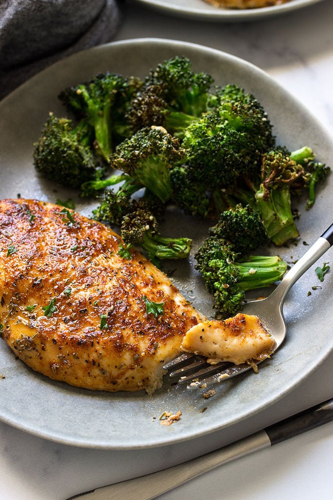 An oven-baked chicken breast on a gray plate with a side of crispy broccoli.