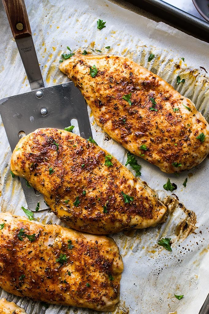 Three freshly baked chicken breasts on parchment paper on a baking sheet.
