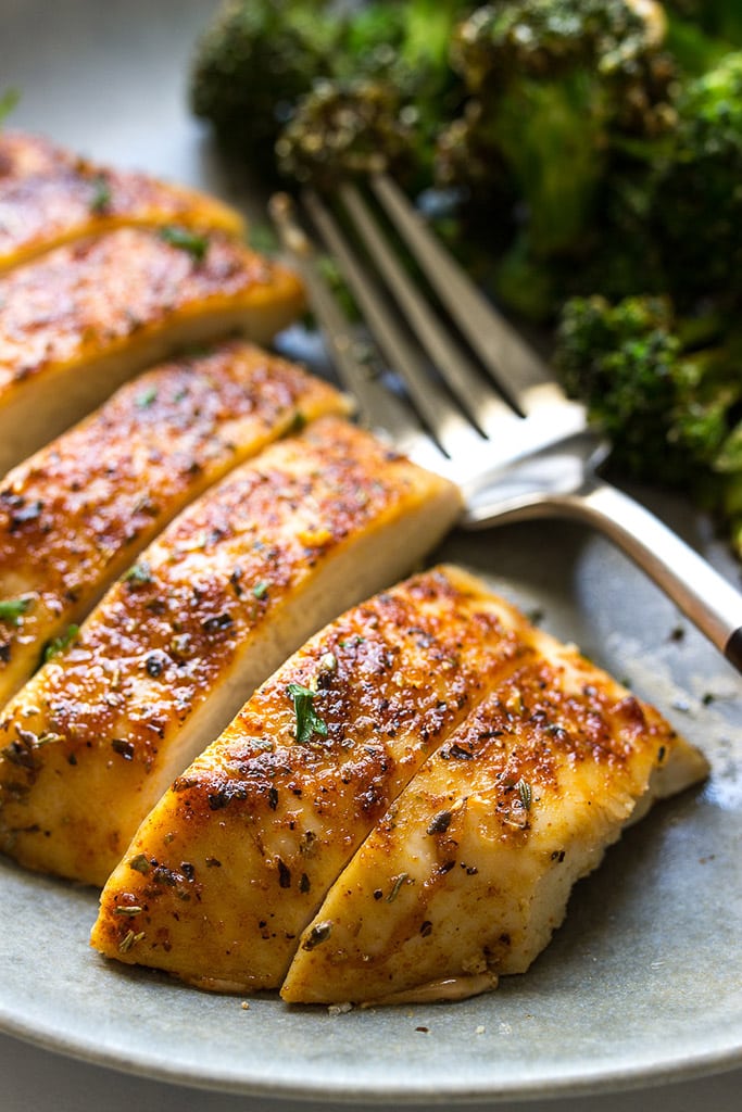 A sliced chicken breast on a gray plate with a side of broccoli.