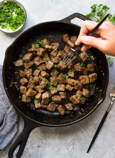 Some garlic butter steak bites in a cast iron pan topped with fresh parsley.