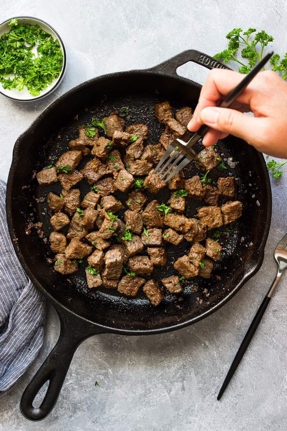 Some garlic butter steak bites in a cast iron pan topped with fresh parsley.