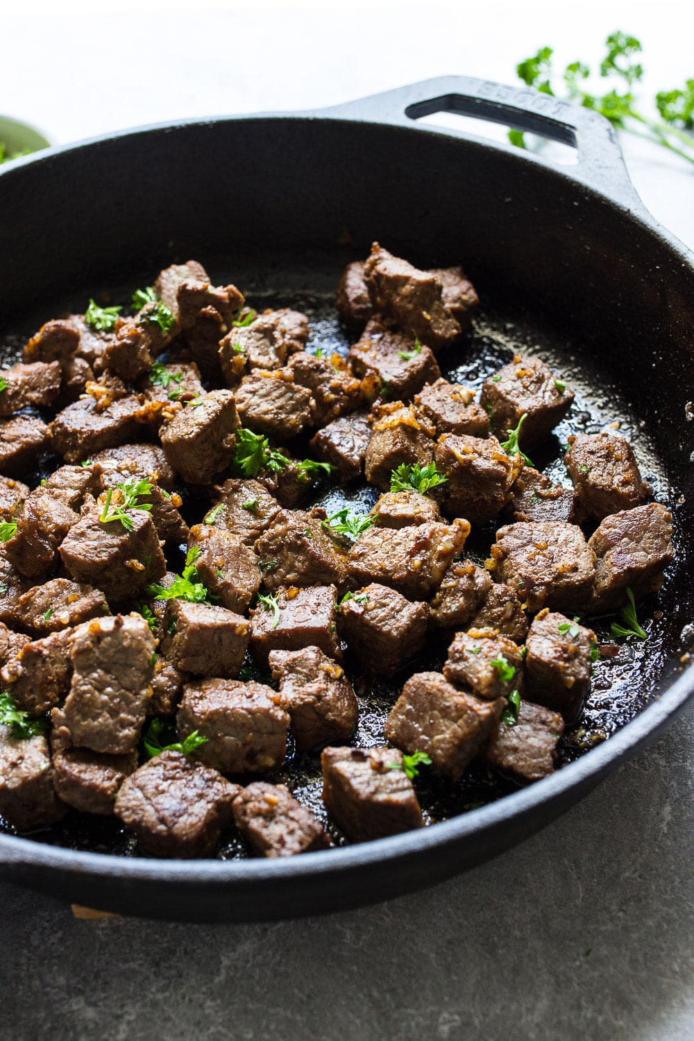 Some garlic butter steak bites in a cast iron pan topped with fresh parsley.