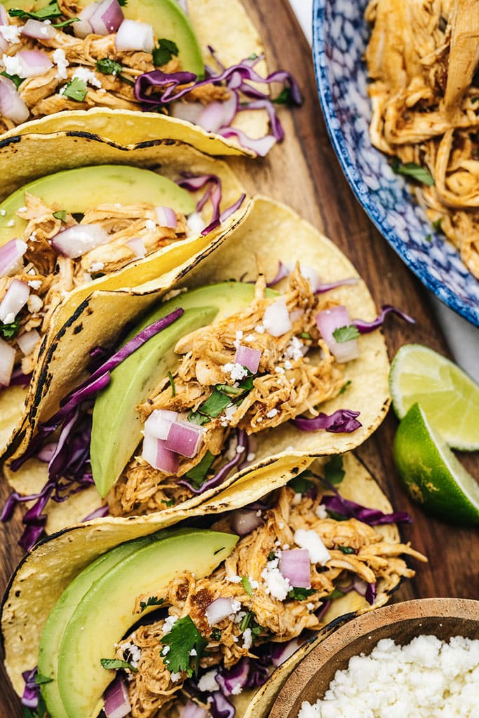 Several chipotle chicken tacos on charred corn tortillas with purple cabbage, avocado, red onions, cilantro and limes.