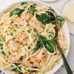 A plate of creamy salmon pasta with lemon wedges and grated Parmesan cheese on the side.