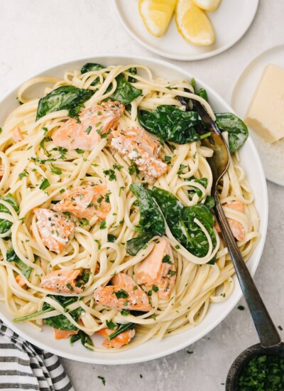 A plate of creamy salmon pasta with lemon wedges and grated Parmesan cheese on the side.