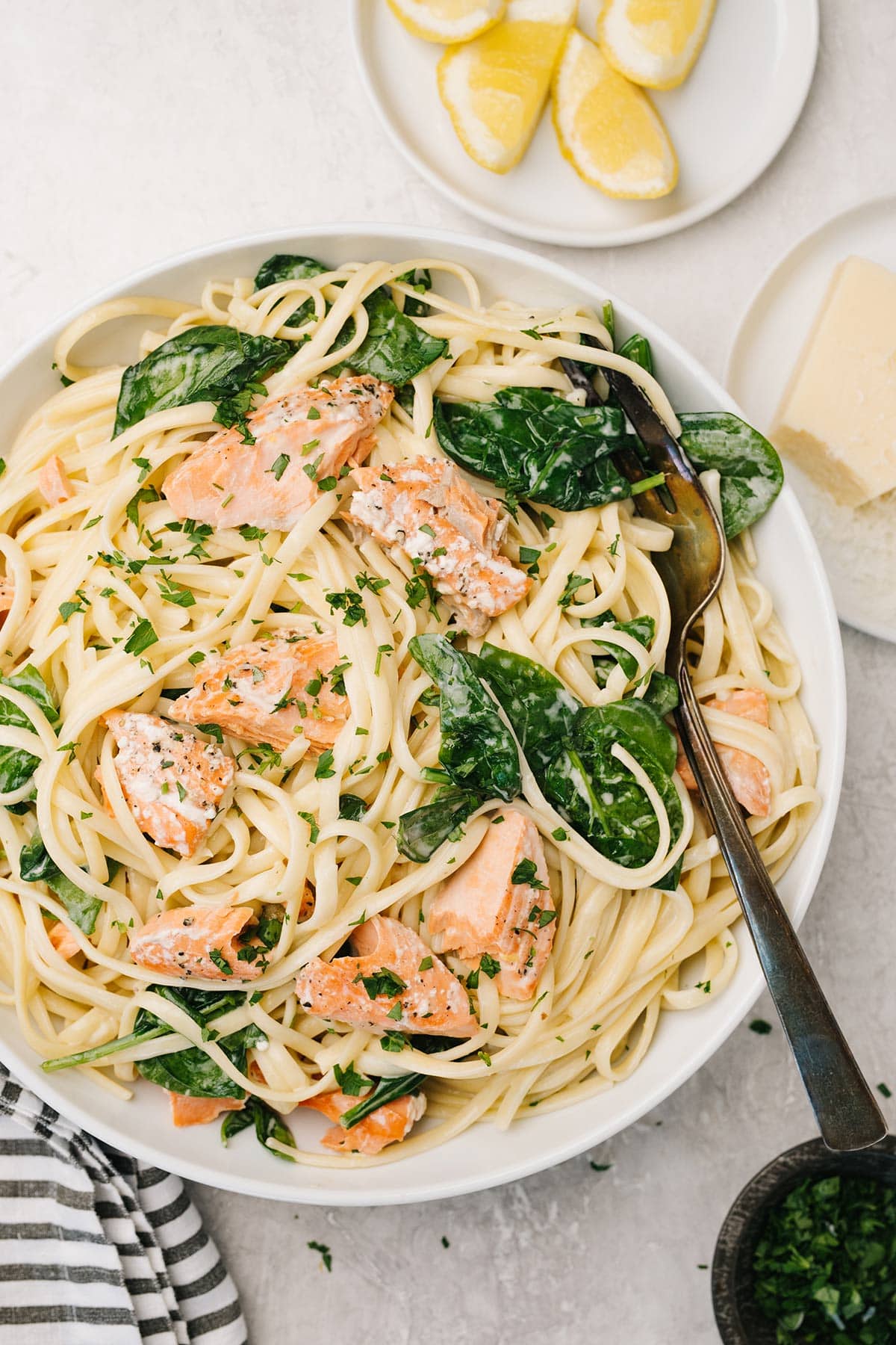 A plate of creamy salmon pasta with spinach with lemon wedges and grated Parmesan cheese on the side.