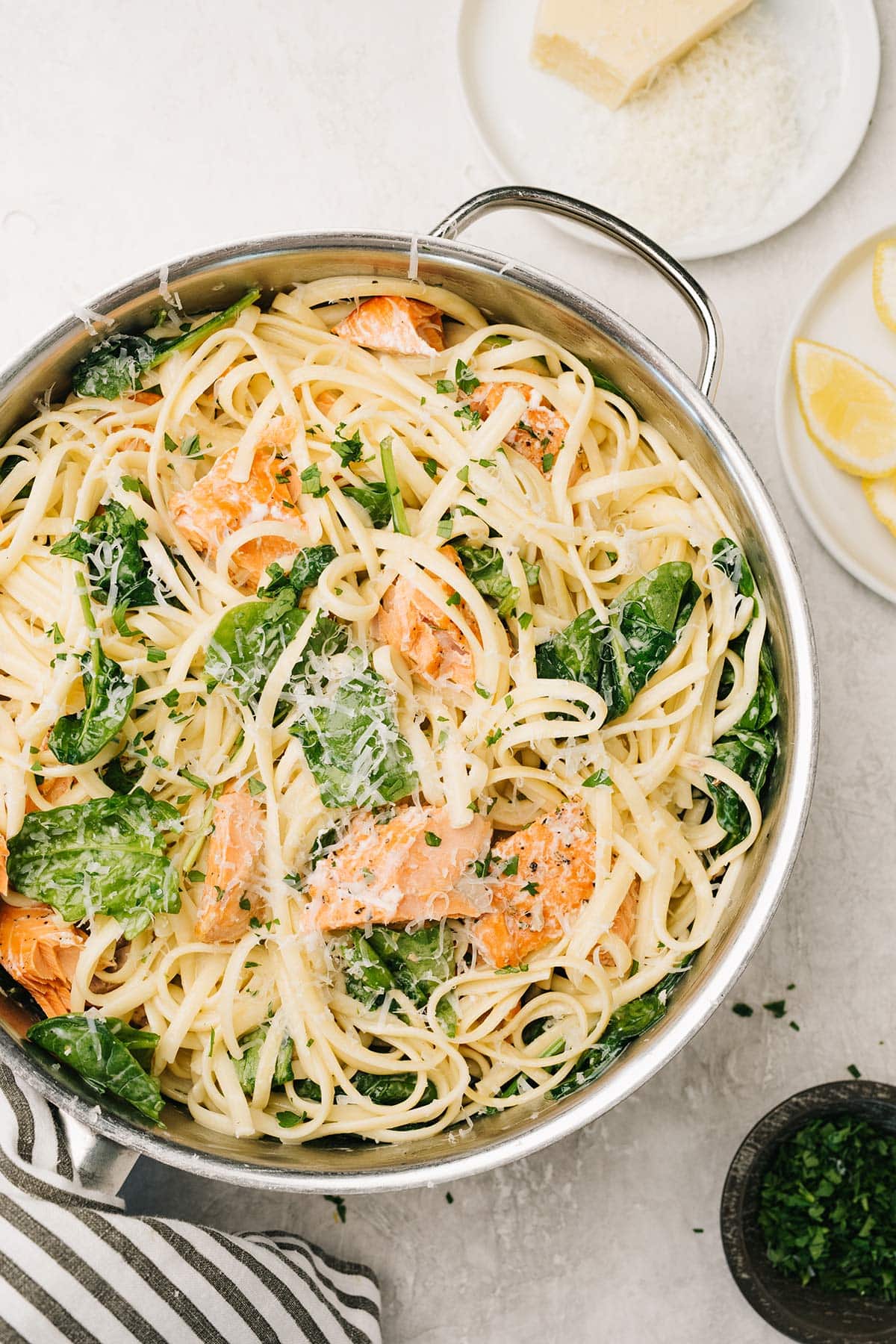 Creamy salmon pasta with spinach in a saucepan with lemon wedges and Parmesan cheese on the side.