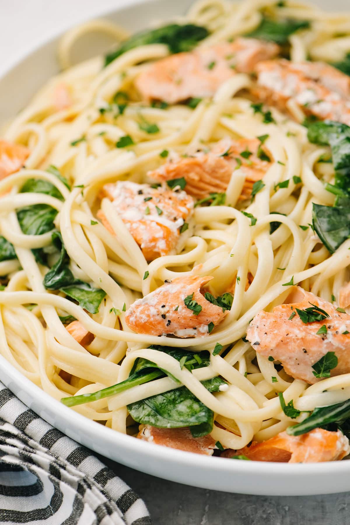 A close up shot of creamy salmon pasta with spinach on a white plate.