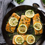 Salmon piccata in a cast iron pan topped with capers, lemon slices and fresh parsley.