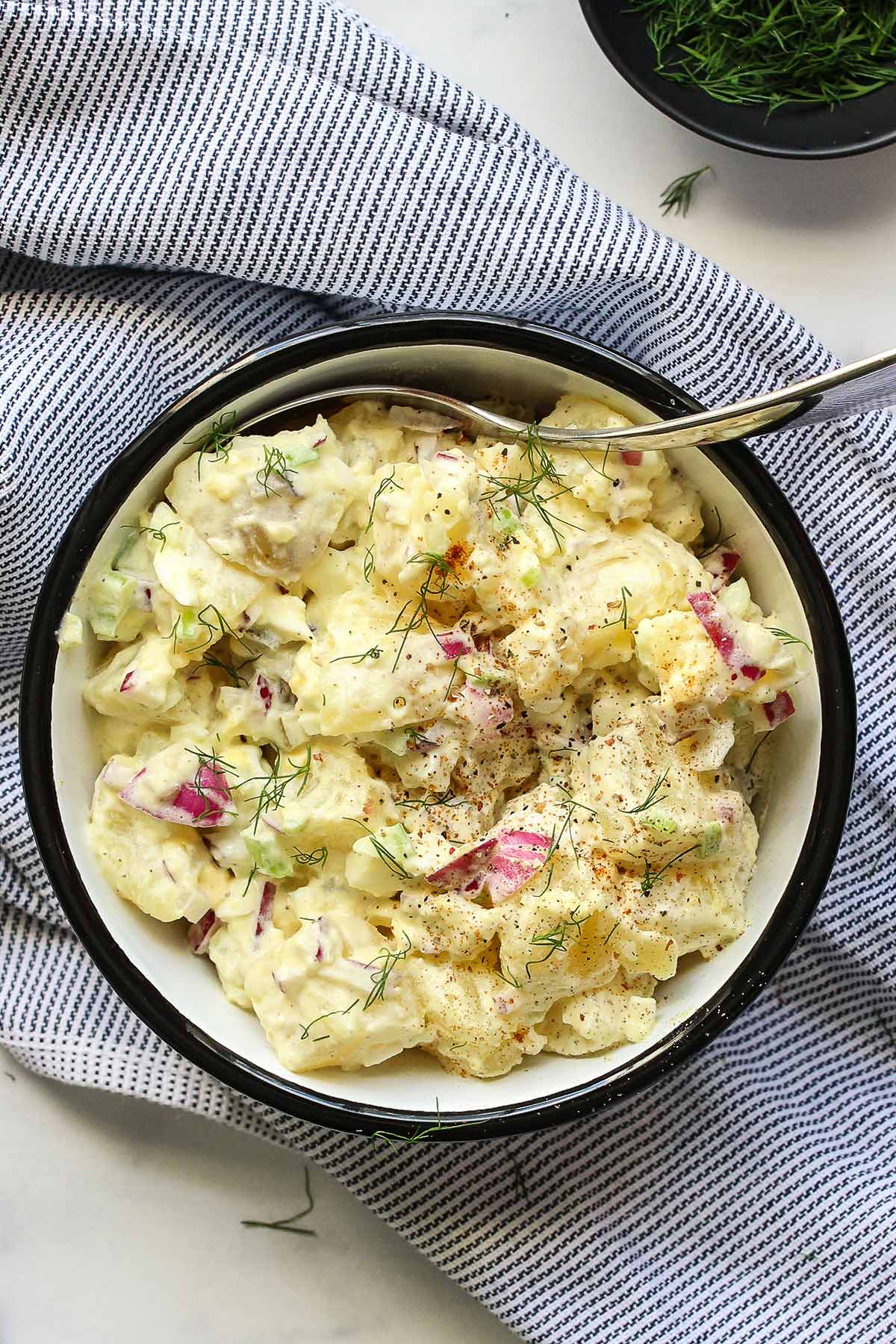 A creamy potato salad topped with fresh dill in white bowl.
