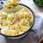 A creamy potato salad topped with fresh dill in white bowl.