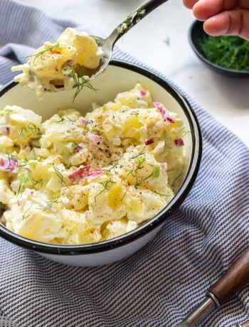 A creamy potato salad topped with fresh dill in white bowl.