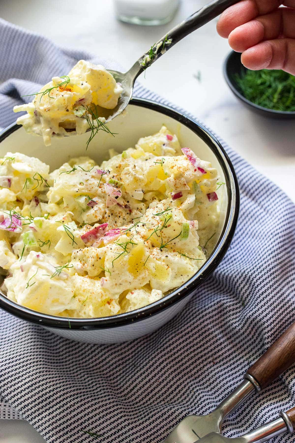 A creamy potato salad topped with fresh dill in white bowl.