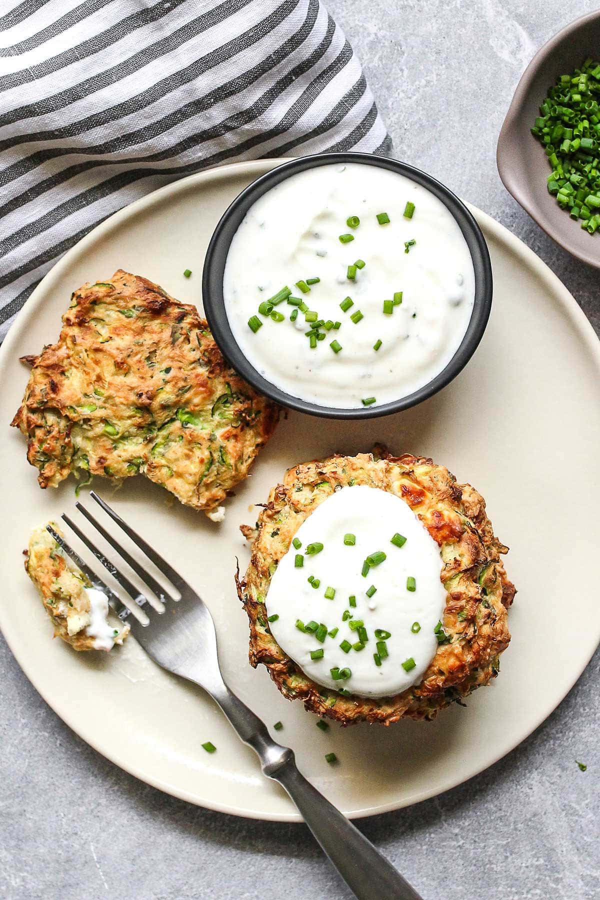 Some air fryer zucchini fritters on a white plate with a yogurt dip and fresh chives.