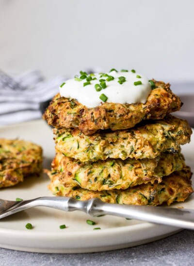 Some air fryer zucchini fritters on a white plate with a yogurt dip and fresh chives.