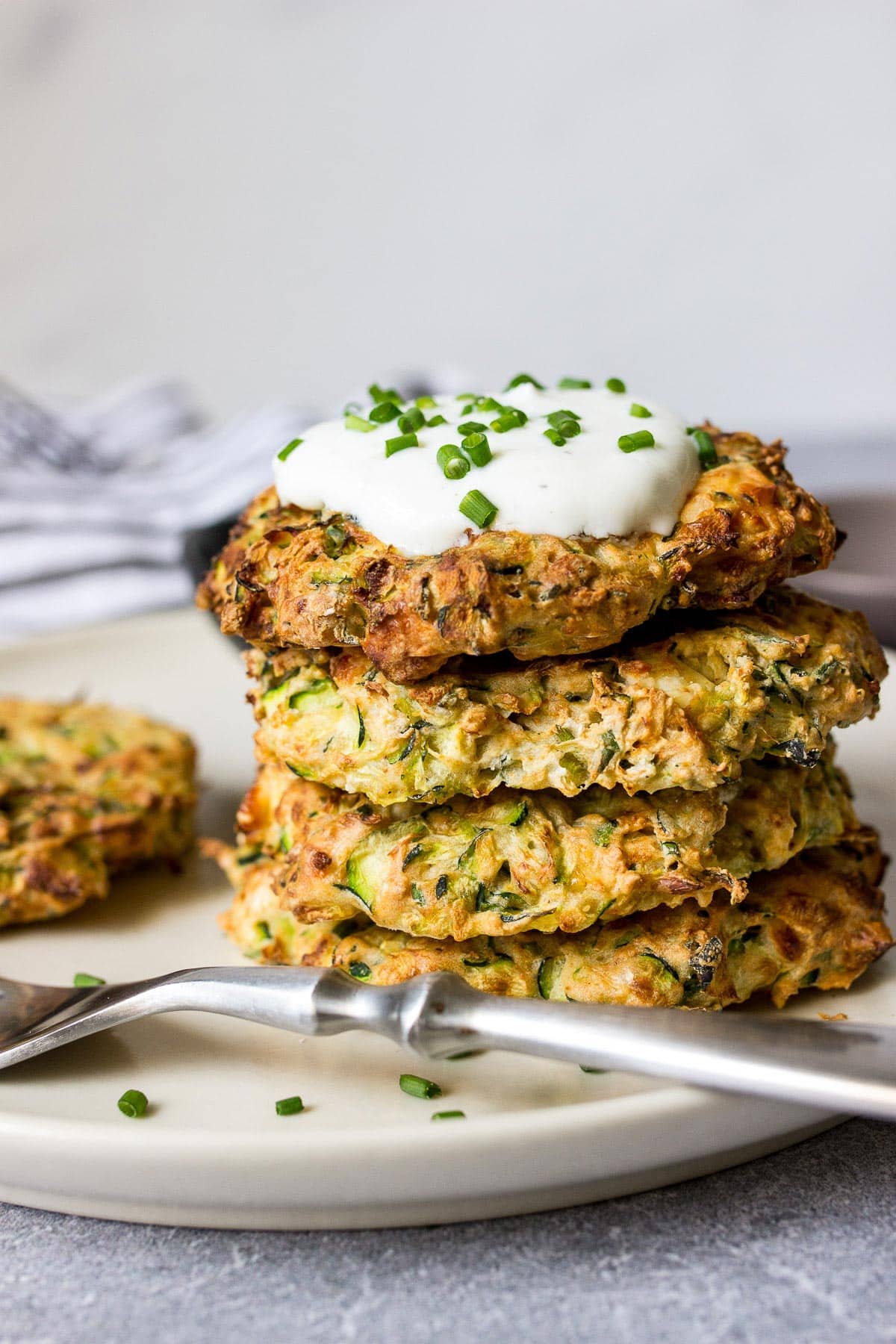 Some air fryer zucchini fritters on a white plate with a yogurt dip and fresh chives.