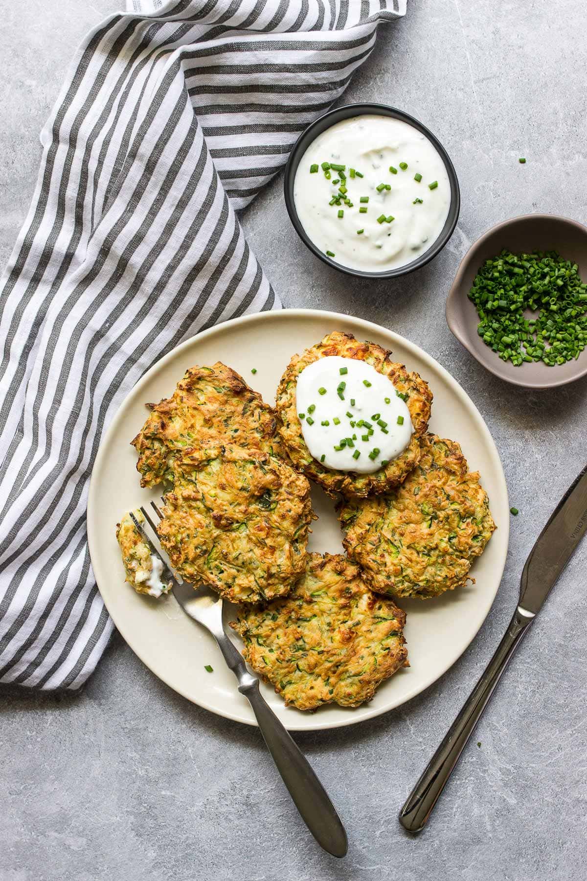 Some air fryer zucchini fritters on a white plate with a yogurt dip and fresh chives.