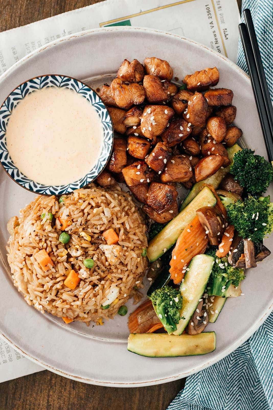 Hibachi rice, chicken and veggies on a white plate with some yum yum sauce on the side.
