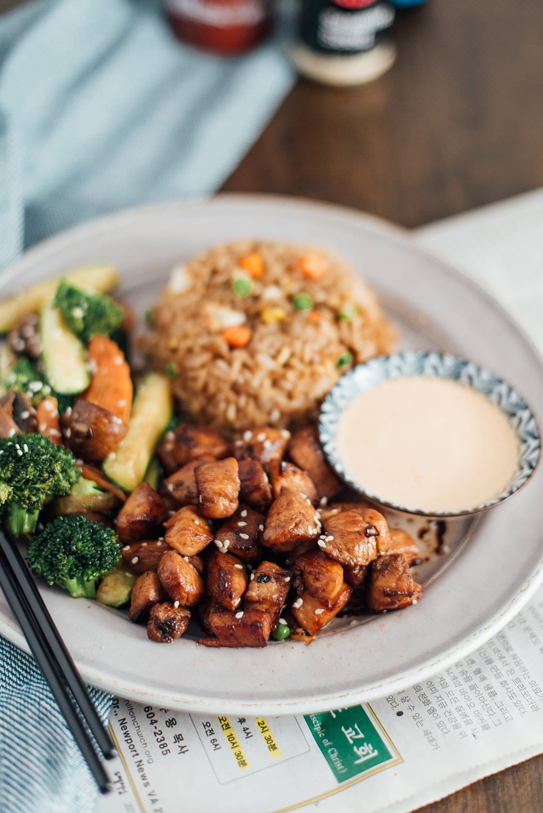 Hibachi rice, chicken and veggies on a white plate with some yum yum sauce on the side.