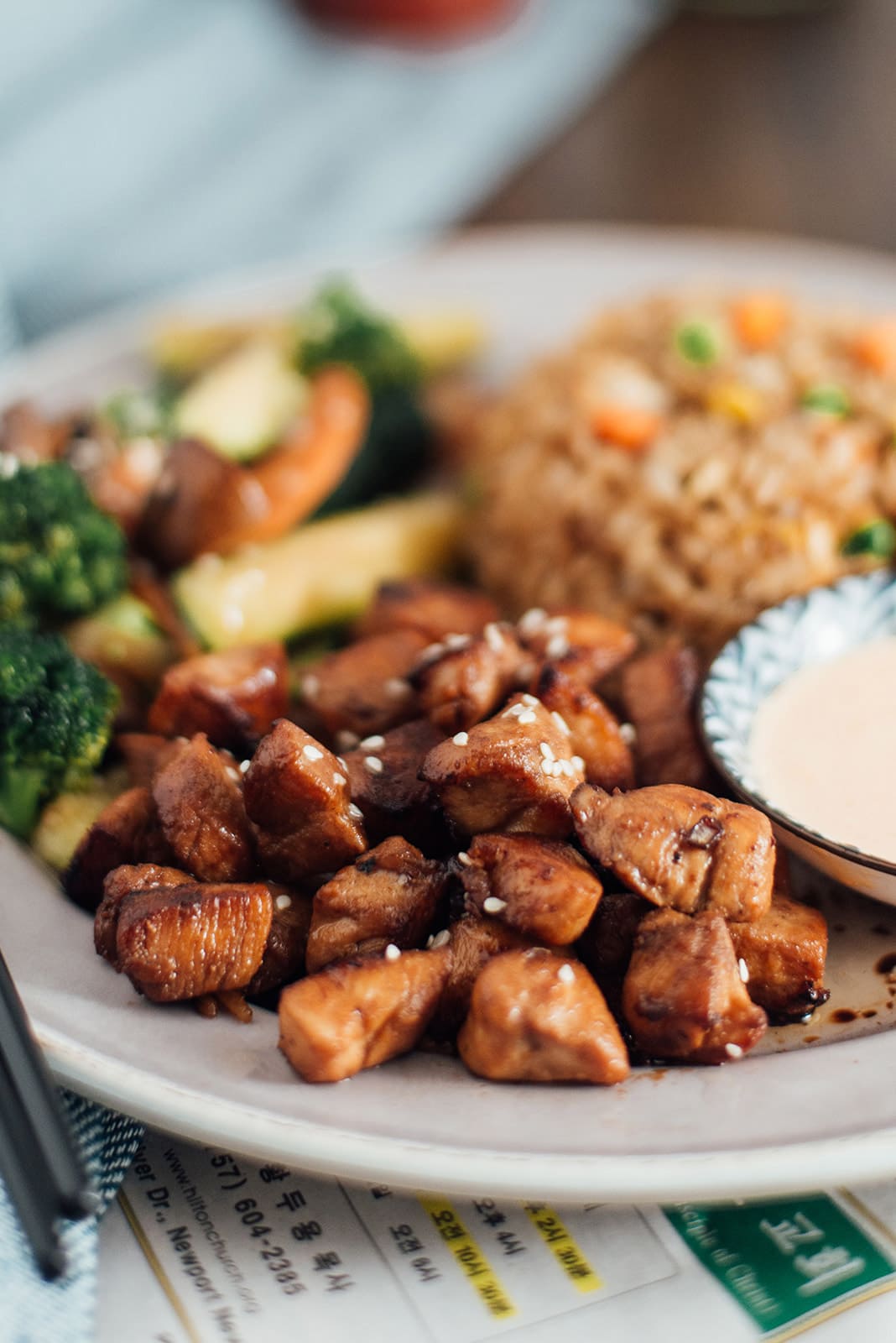 A close up shot of hibachi chicken with hibachi rice and vegetables in the background.