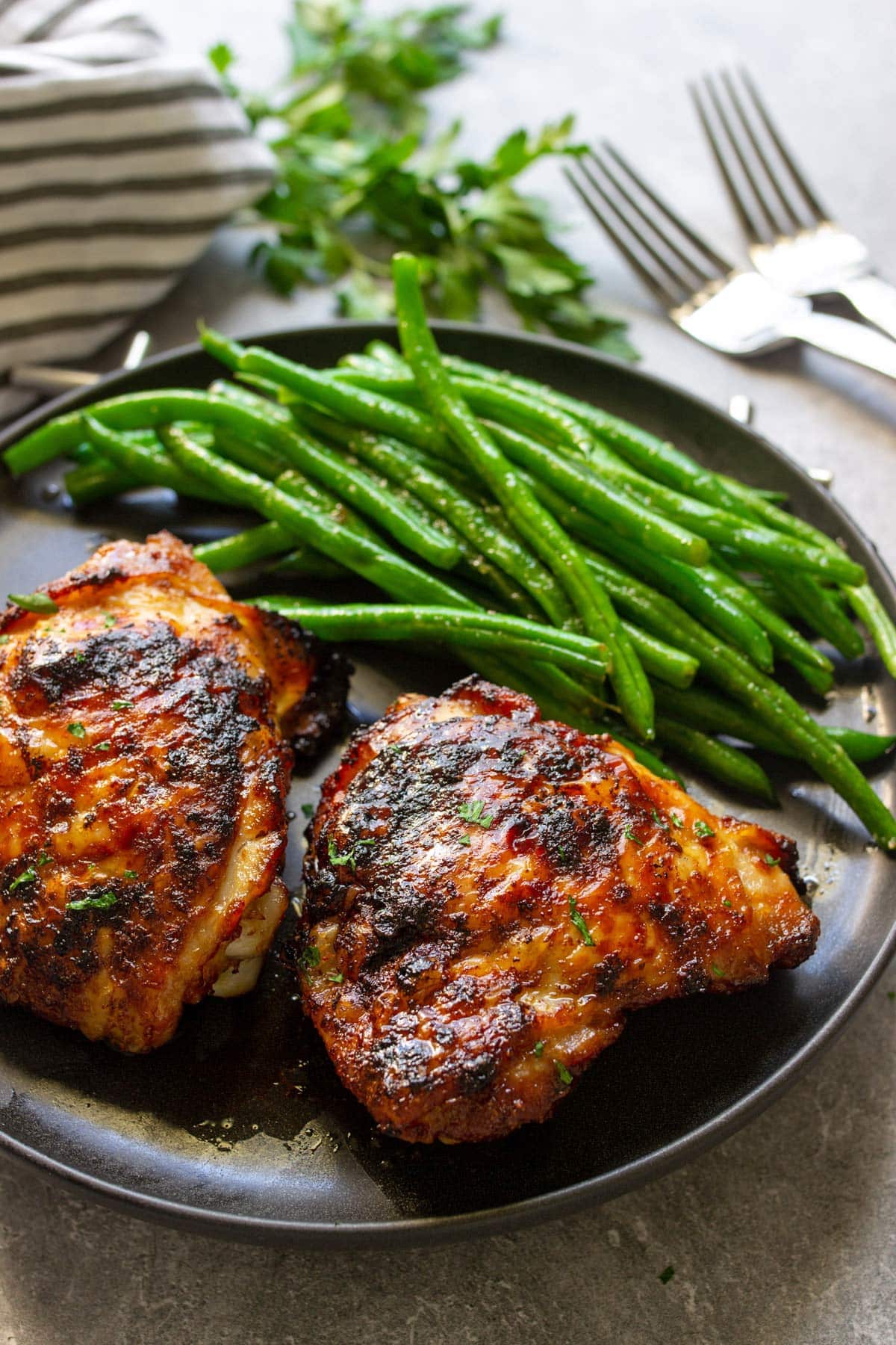 A black plate full of crispy air fryer maple chicken thighs with some green beans.