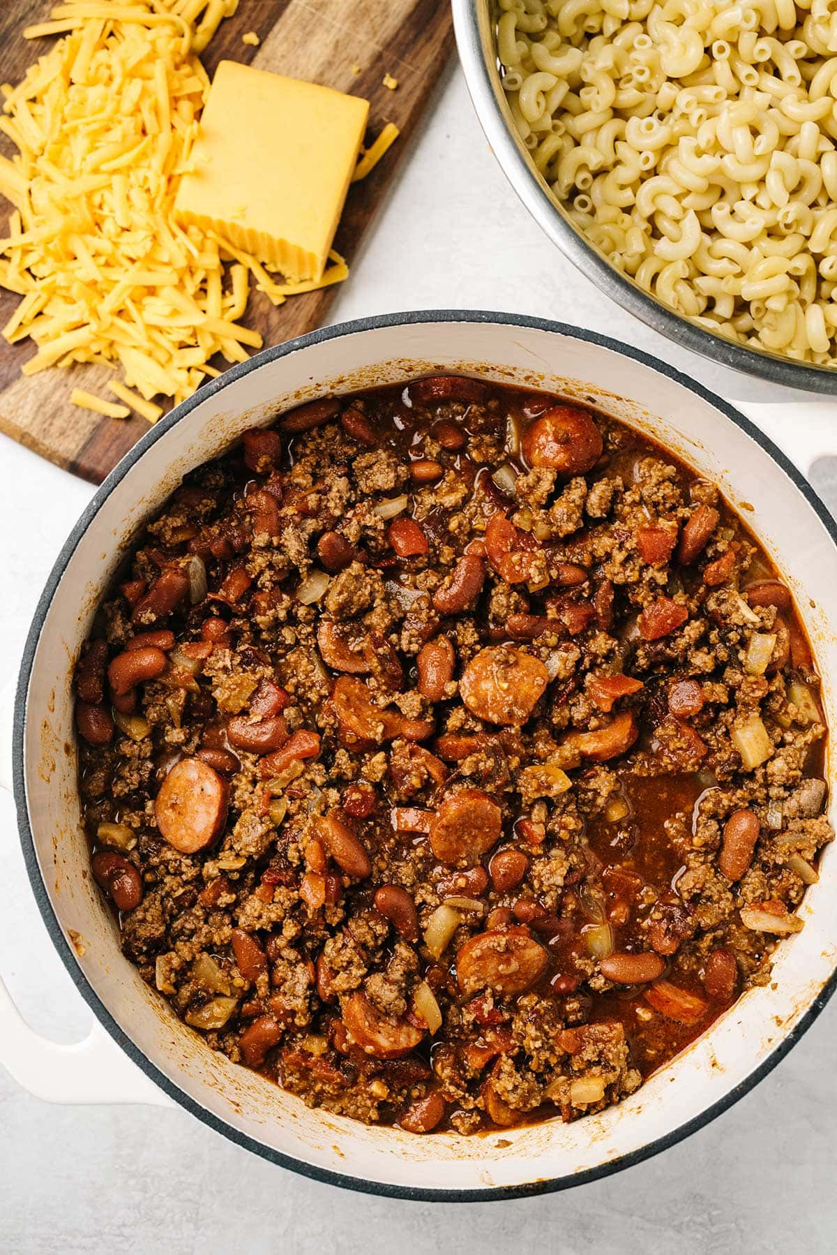 Preparation of chipotle chili mac and cheese with a pot full of chili beans and beef with cooked pasta and cheese on the side.