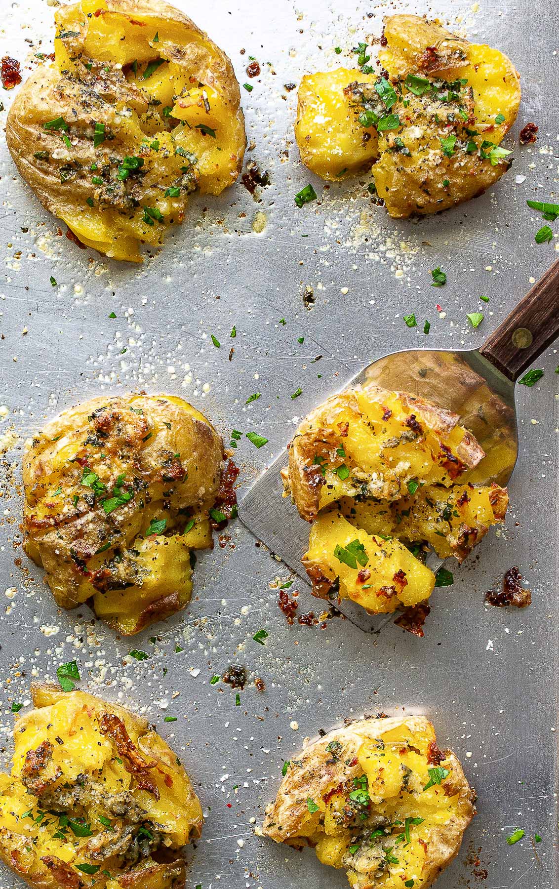 Crispy garlic Parmesan smashed potatoes on a baking sheet topped with fresh parsley.