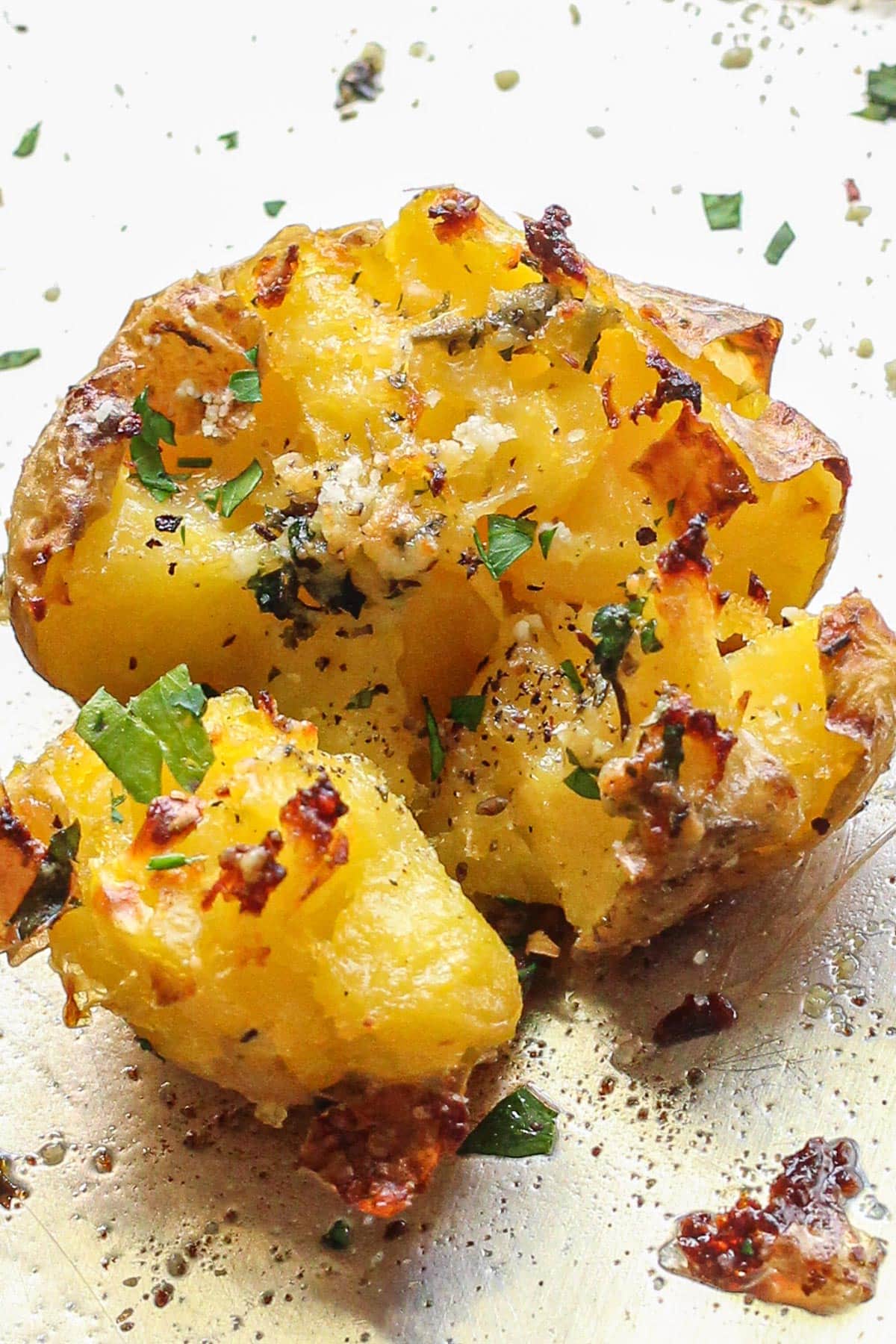 Crispy garlic Parmesan smashed potatoes on a baking sheet topped with fresh parsley.