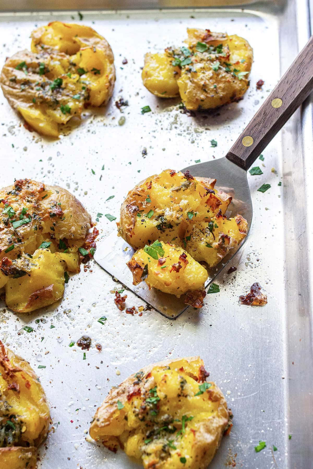 Crispy garlic Parmesan smashed potatoes on a baking sheet topped with fresh parsley.