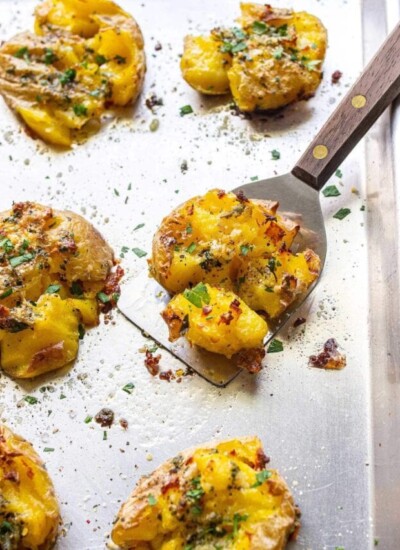 Crispy garlic Parmesan smashed potatoes on a baking sheet topped with fresh parsley.