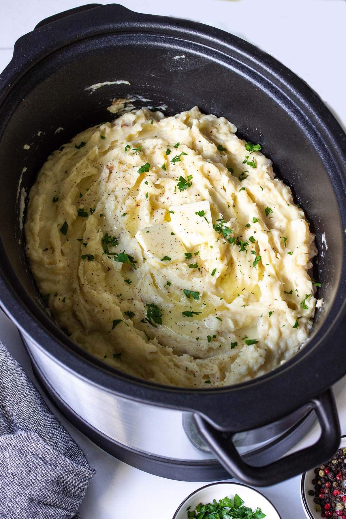 Mashed potatoes in a slow cooker topped with butter cubes and fresh parsley.