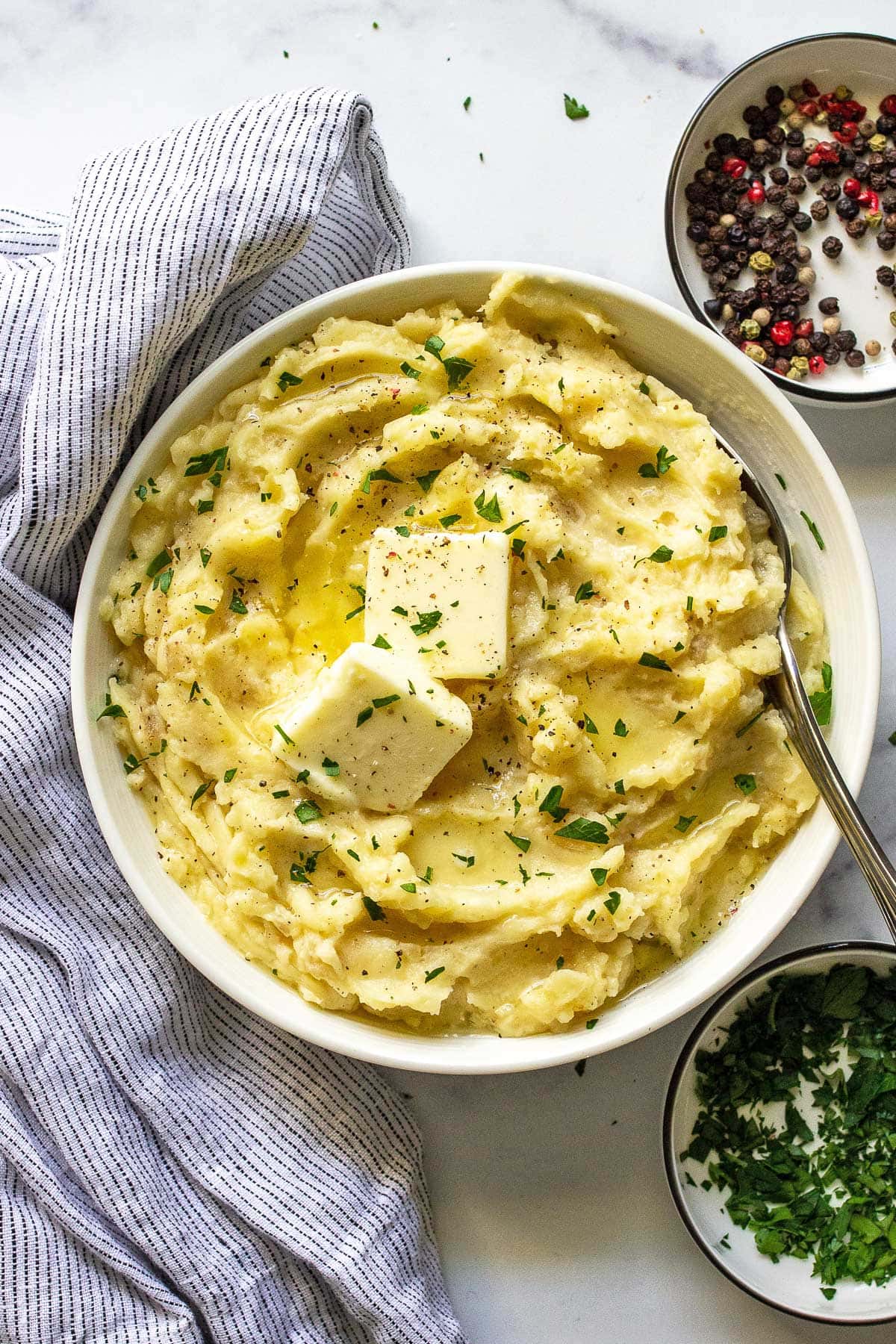 A white bowl of mashed potatoes with slabs of butter and fresh parsley on top.