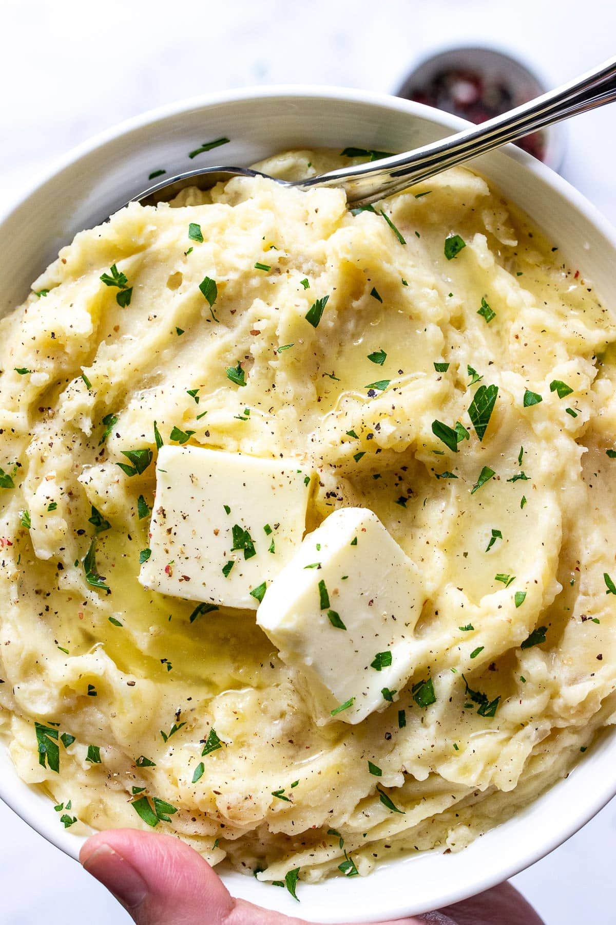 A white bowl of mashed potatoes with slabs of butter and fresh parsley on top.