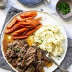 A plate of shredded chuck roast with mashed potatoes and carrots topped with fresh parsley.